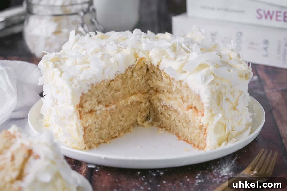 Coconut Cake Without Gluten: Moist Recipe for Allergy-Friendly Celebrations 19 Gluten-Free Coconut Cake covered in coconut flakes on a white plate. Cut into showing soft moisture texture.
