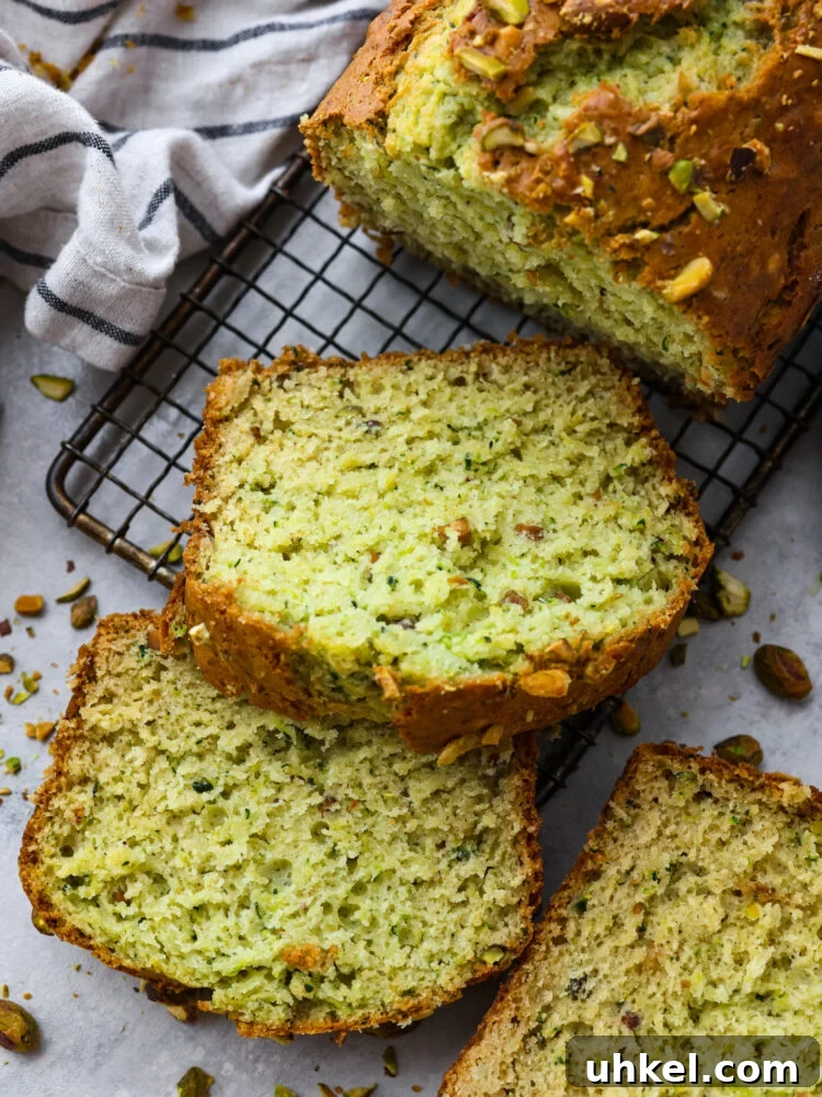 This deliciously soft pistachio zucchini bread is the perfect twist on a classic recipe. Packed with tons of unique flavor combinations from the pistachios and zucchini, you will LOVE this bread! A loaf of pistachio bread on a cooling rack with the end sliced.
