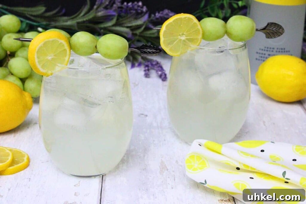 Cîroc Lemonade Spritzer Recipe — Refreshing Vodka Limonata Spritz 8 two vodka lemonade spritzers garnished with lemon and grape on a white wooden table