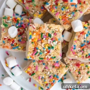 Overhead view of birthday cake rice krispie treats on white plate with sprinkles and marshmallows.