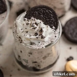 Oreo cheesecake cups topped with whipped cream and an Oreo along with more cookie crumbs.