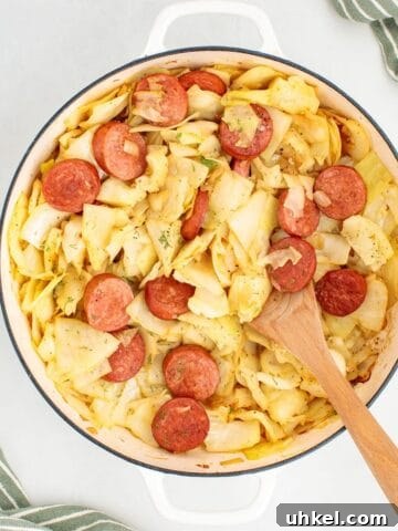 A cooked skillet dinner made with sliced kielbasa and tender cabbage, with a wooden spoon for serving.