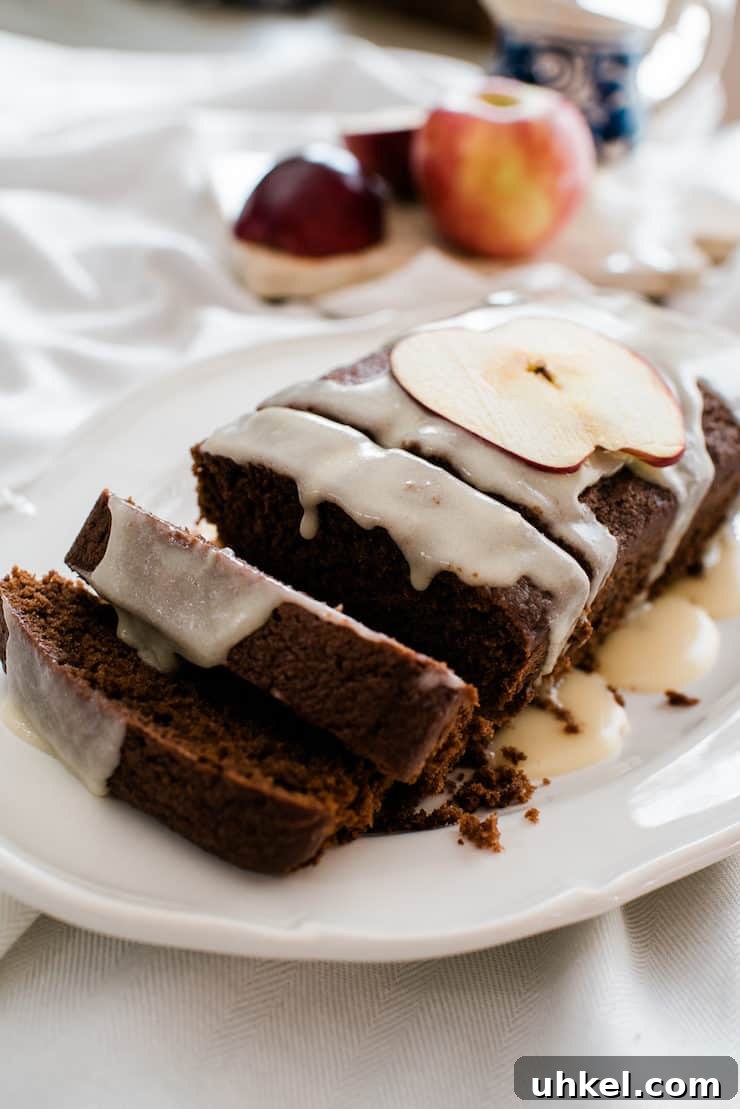 Moist Chocolate Loaf with Bourbon Glaze Recipe 2 sliced chocolate apple bread drizzled with a sweet boozy bourbon glaze on a white plate with apples in the background