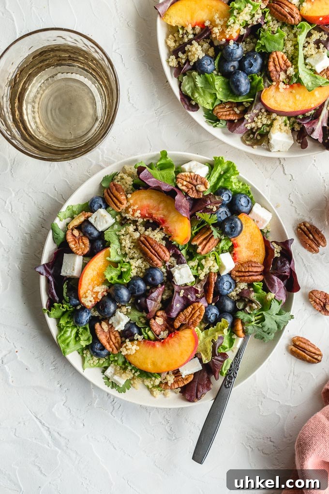 Overhead view of summer peach salad on white plates on a white surface.