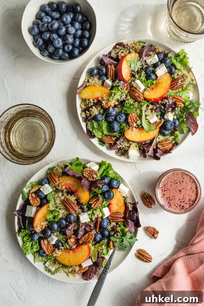 Two plates filled with peach blueberry salad with dressing off to the side.