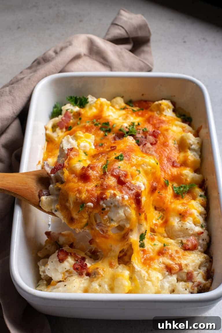 A serving spoon scooping up a portion of loaded cauliflower casserole showing the cheesy texture.