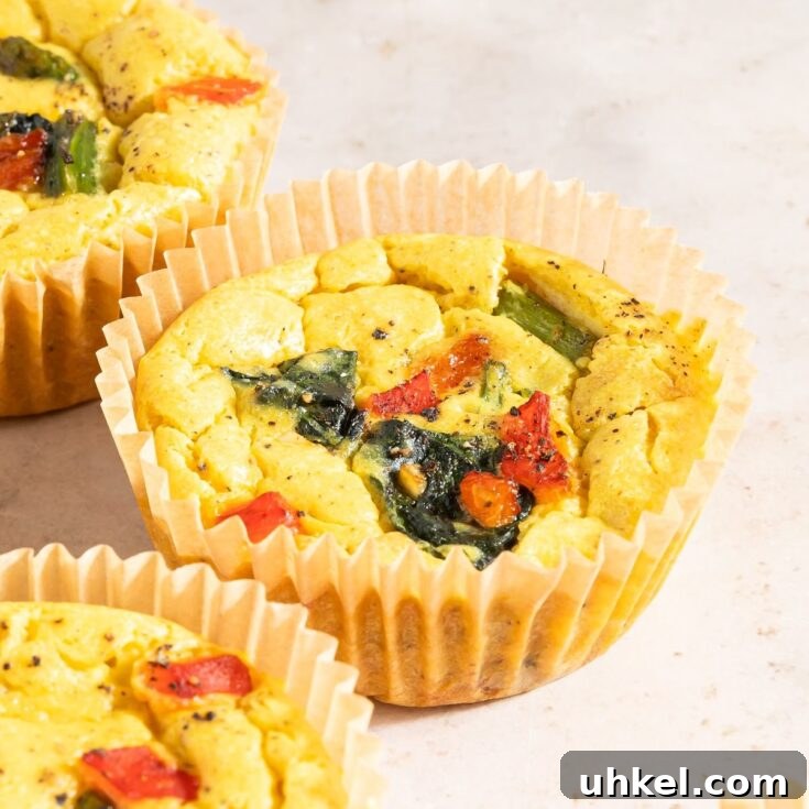 Close up of mini vegan quiche on an off white countertop. The vegan egg bites are bright yellow from turmeric, and are filled with red peppers, spinach, and asparagus.