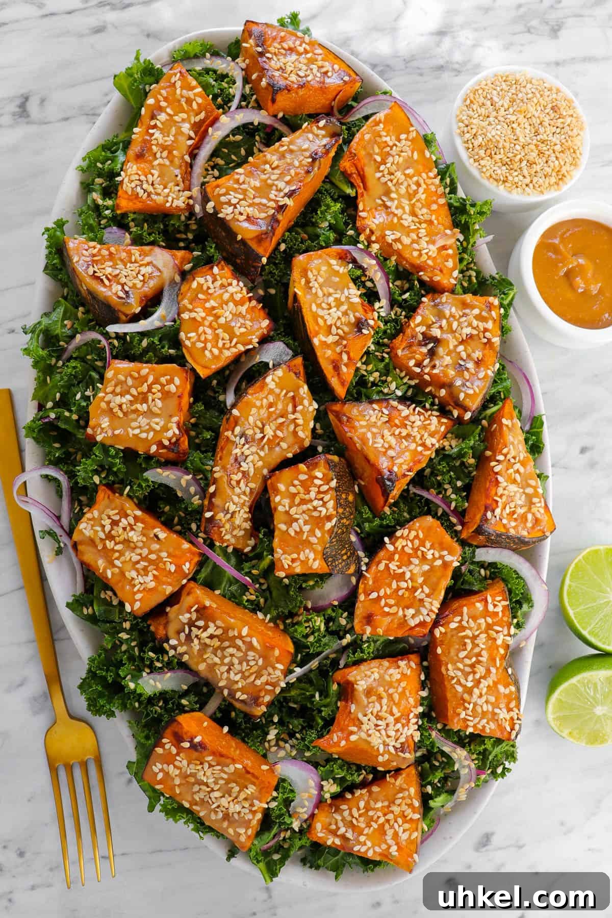 Miso-Glazed Pumpkin and Kale Salad with Toasted Seeds 2 Pumpkin salad with fork, limes, sesame seeds and tahini miso sauce on the side.