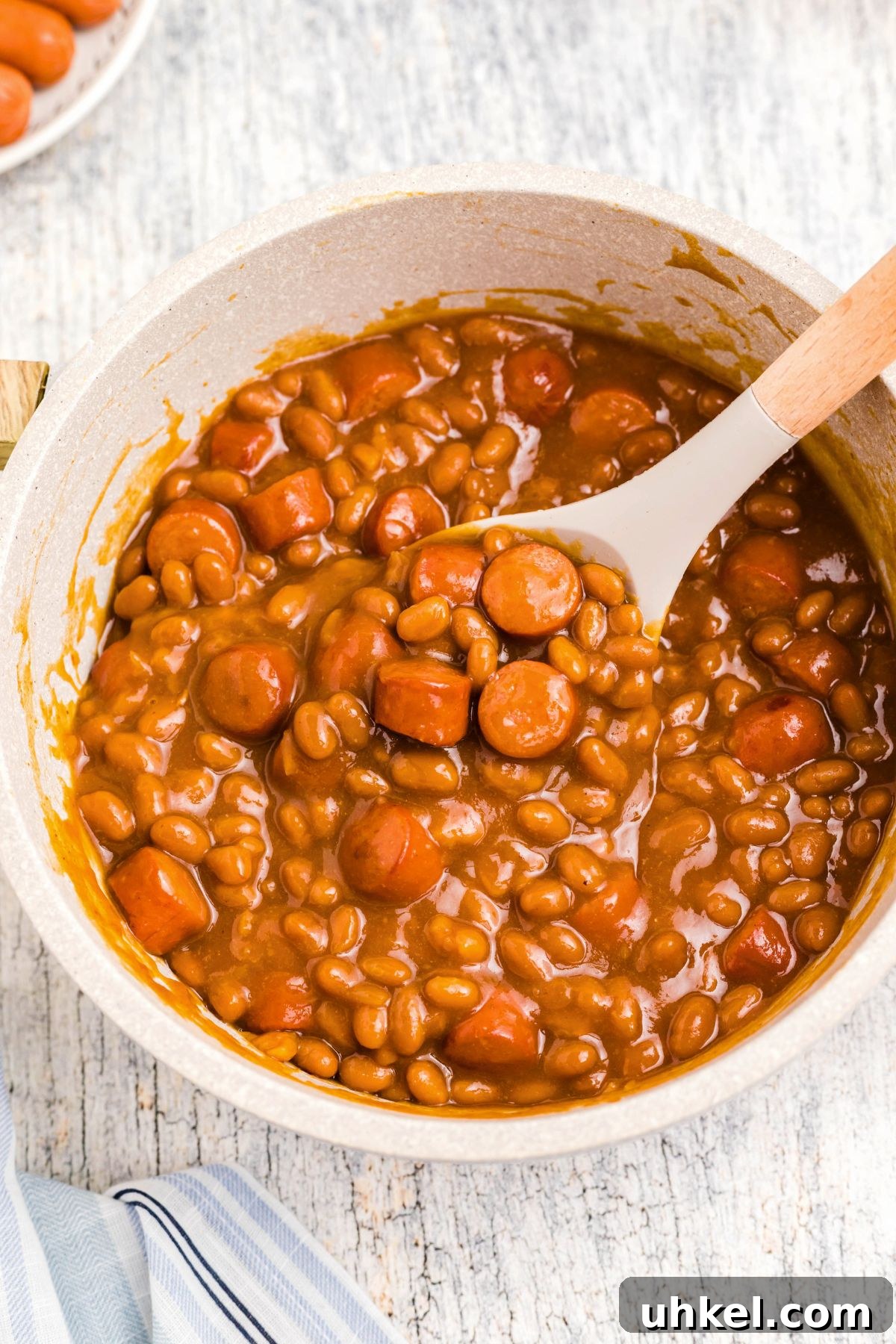 Classic Beanie Weenies Recipe with Flavorful Tomato Sauce 2 Juicy Beanie weenies being scooped up out of a large saucepan.
