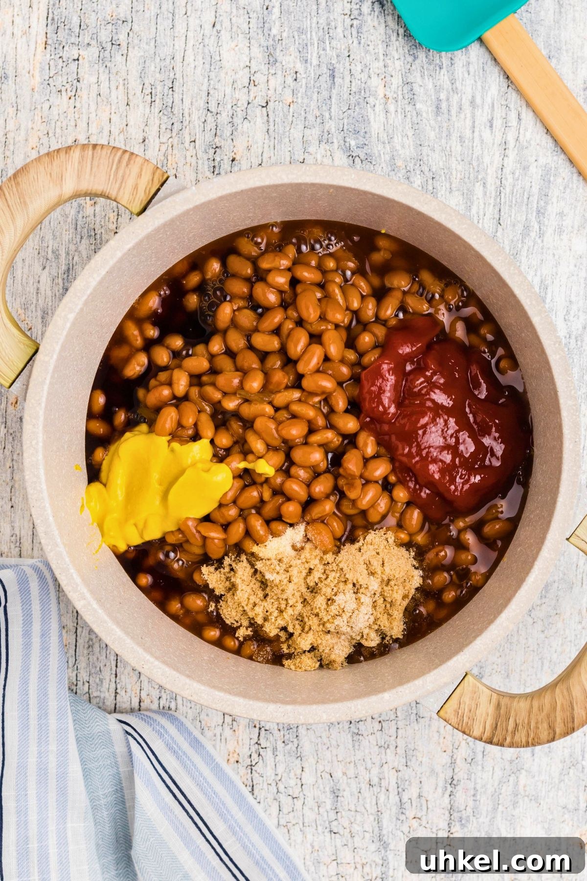 Classic Beanie Weenies Recipe with Flavorful Tomato Sauce 5 Mustard, ketchup and other ingredients being added to saucepan.
