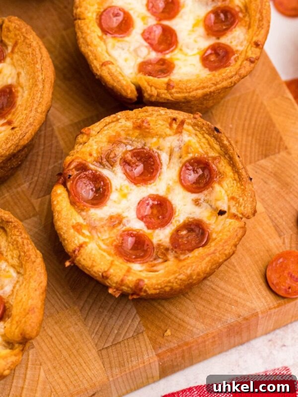 Classic Beanie Weenies Recipe with Flavorful Tomato Sauce 10 Golden crusted pizza cupcakes on a wooden cutting board with pepperoni scattered around the table.