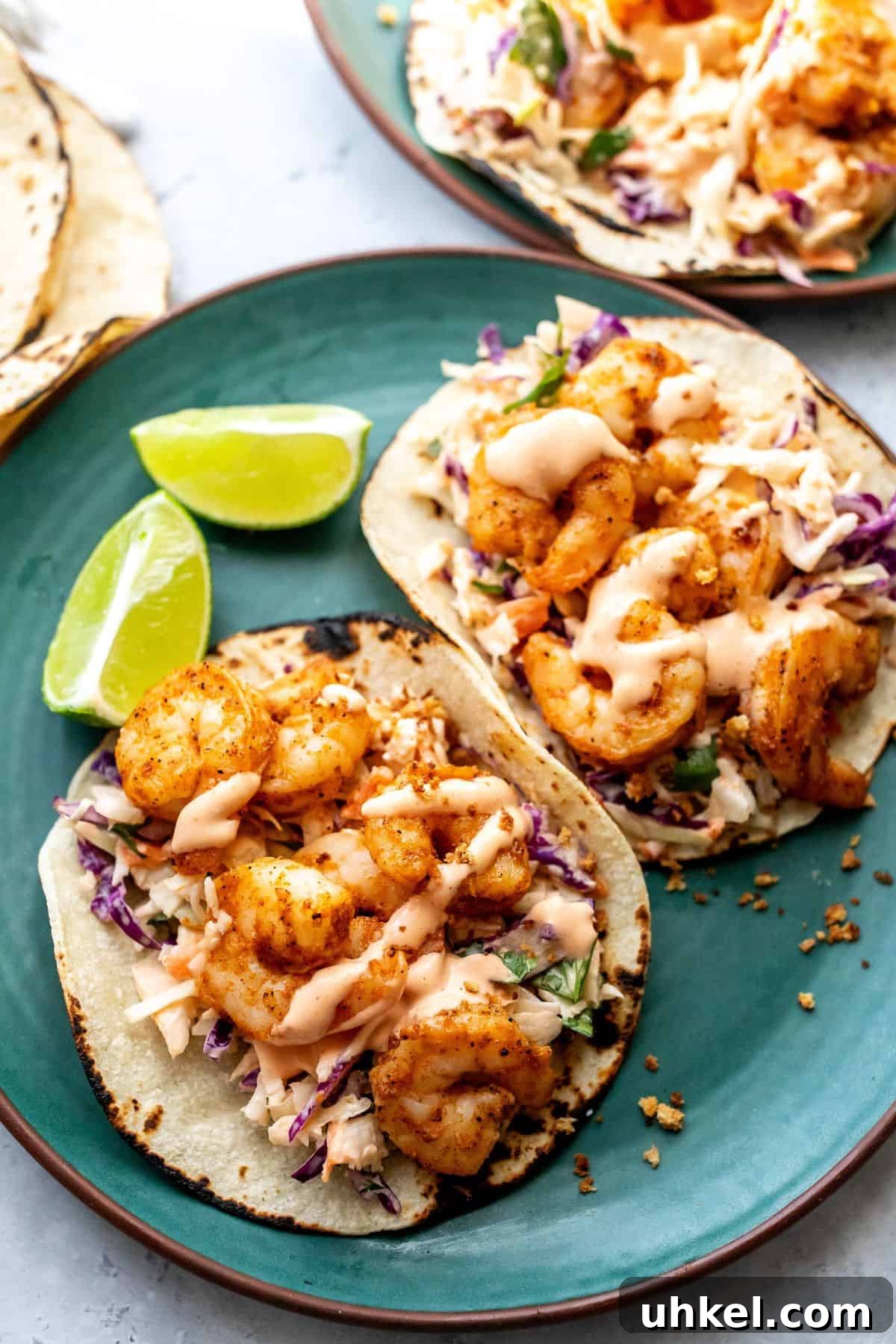 Crispy Baja Shrimp Tacos with Tangy Lime Slaw 2 Baja shrimp tacos on a green plate with limes on the side.