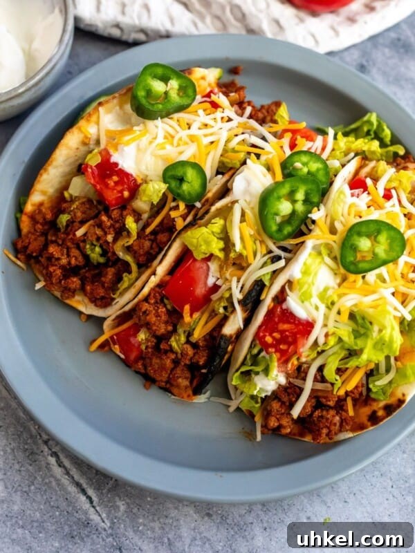 Crispy Baja Shrimp Tacos with Tangy Lime Slaw 8 Beef soft tacos on a gray plate with cheese, lettuce, and jalapenos.