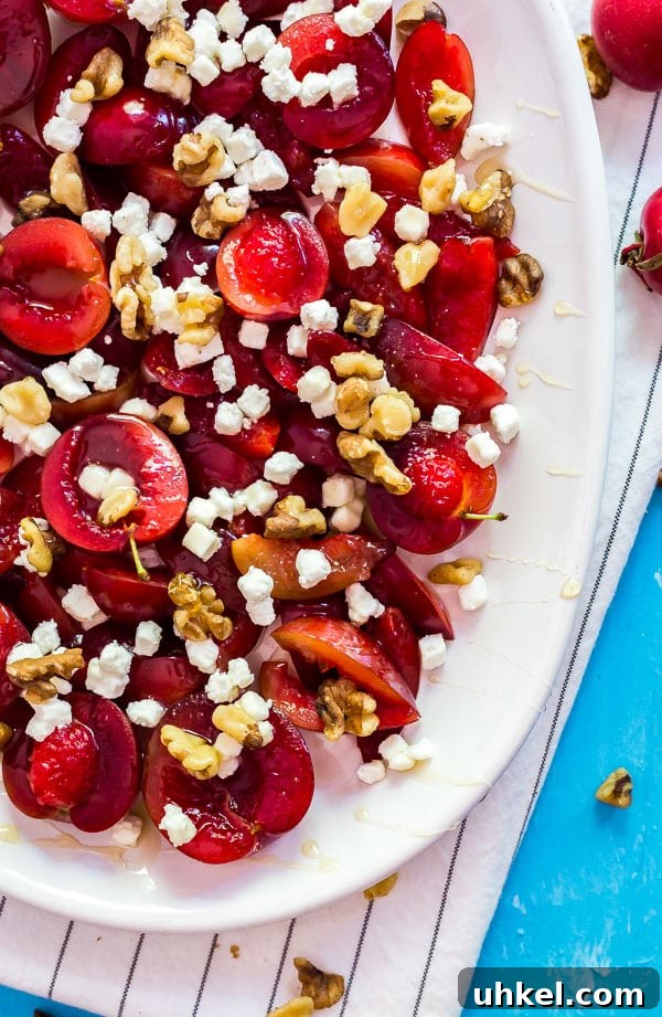 Roasted Plums with Goat Cheese and Toasted Walnuts 2 An over head image of the bottom of a plate of plums with goat cheese and walnuts on a white cloth and blue background.