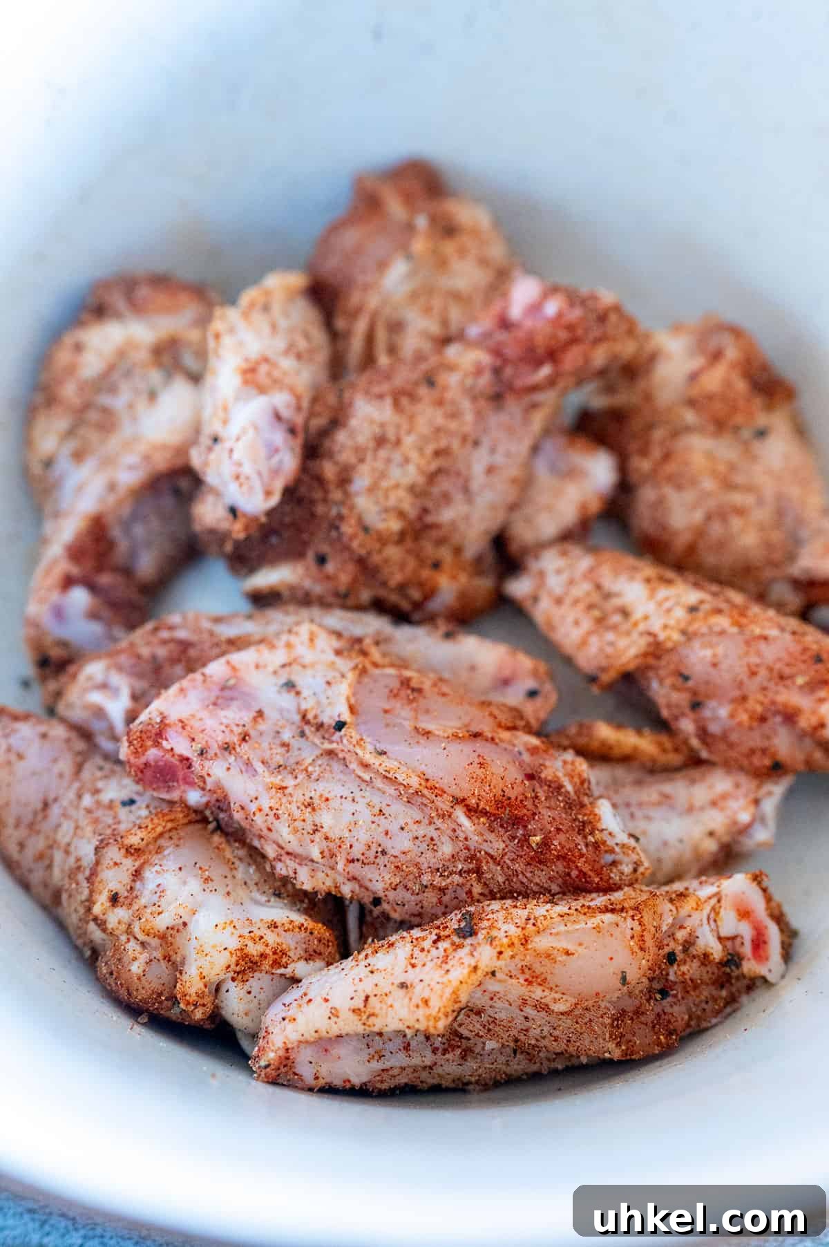 Savory Homemade Dry Rub Recipe for Crispy Chicken Wings 6 Raw chicken wings rubbed with chicken wing dry rub in white bowl.