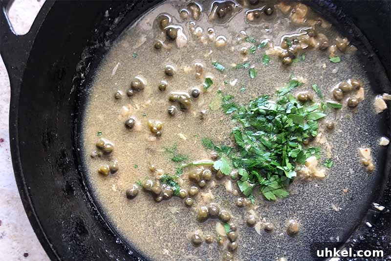 Classic Chicken Piccata with Lemon Butter Sauce Recipe 9 Horizontal image of cooking a sauce with capers and a mound of fresh chopped herbs.