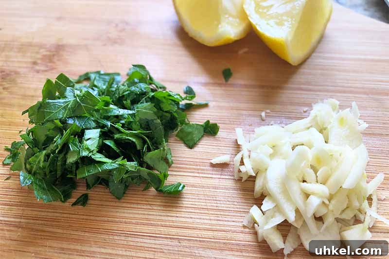 Classic Chicken Piccata with Lemon Butter Sauce Recipe 5 Horizontal image of chopped herbs, garlic, and wedges of citrus on a wooden board.