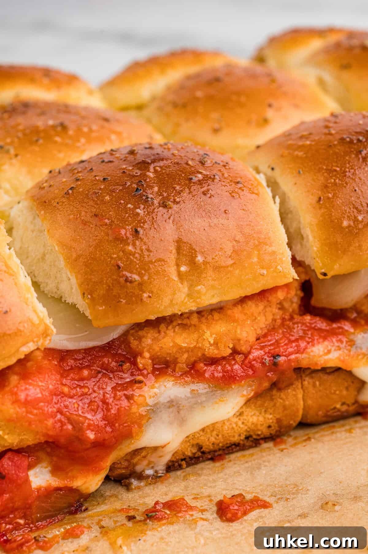 Chicken Parmesan Sliders Recipe: Crispy Mini Sandwiches 6 Close-up of golden brown chicken parm sliders with nuggets in a row, showing layers of breaded chicken, marinara sauce, and melted mozzarella between soft, herb-topped buns.