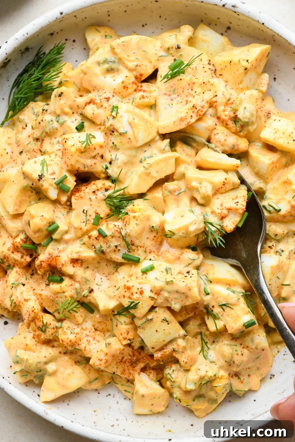 Creamy Deviled Egg Salad Recipe — Ready in 30 Minutes 2 Deviled egg salad in a shallow speckled ceramic bowl with a spoon scooping out some egg salad, garnished with a dash of red paprika, fresh dill, and fresh chives.