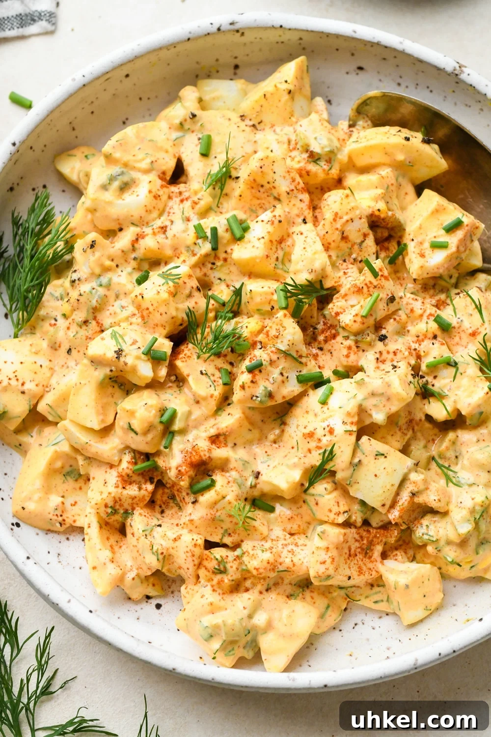 Creamy Deviled Egg Salad Recipe — Ready in 30 Minutes 12 Deviled egg salad in a shallow speckled ceramic bowl, garnished with a dash of red paprika, fresh dill, and fresh chives.