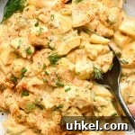 Deviled egg salad in a shallow speckled ceramic bowl with a spoon scooping out some egg salad, garnished with a dash of red paprika, fresh dill, and fresh chives.