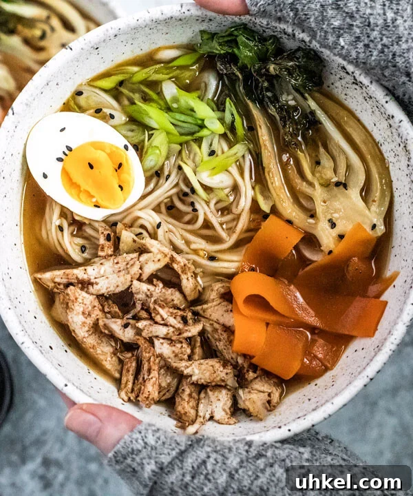 Homemade Ramen Bowl Recipe: Savory Broth & Tasty Toppings 13 Hands holding up five spice chicken Ramen bowl topped with an egg and vegetables.