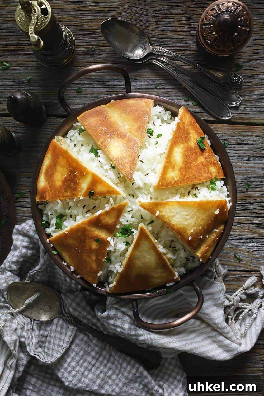 Crispy Tahdig with Naan Crust — Pan-Fried Persian Rice 2 A copper bowl filled with rice and covered with crispy naan bread pieces sitting on a wooden table.