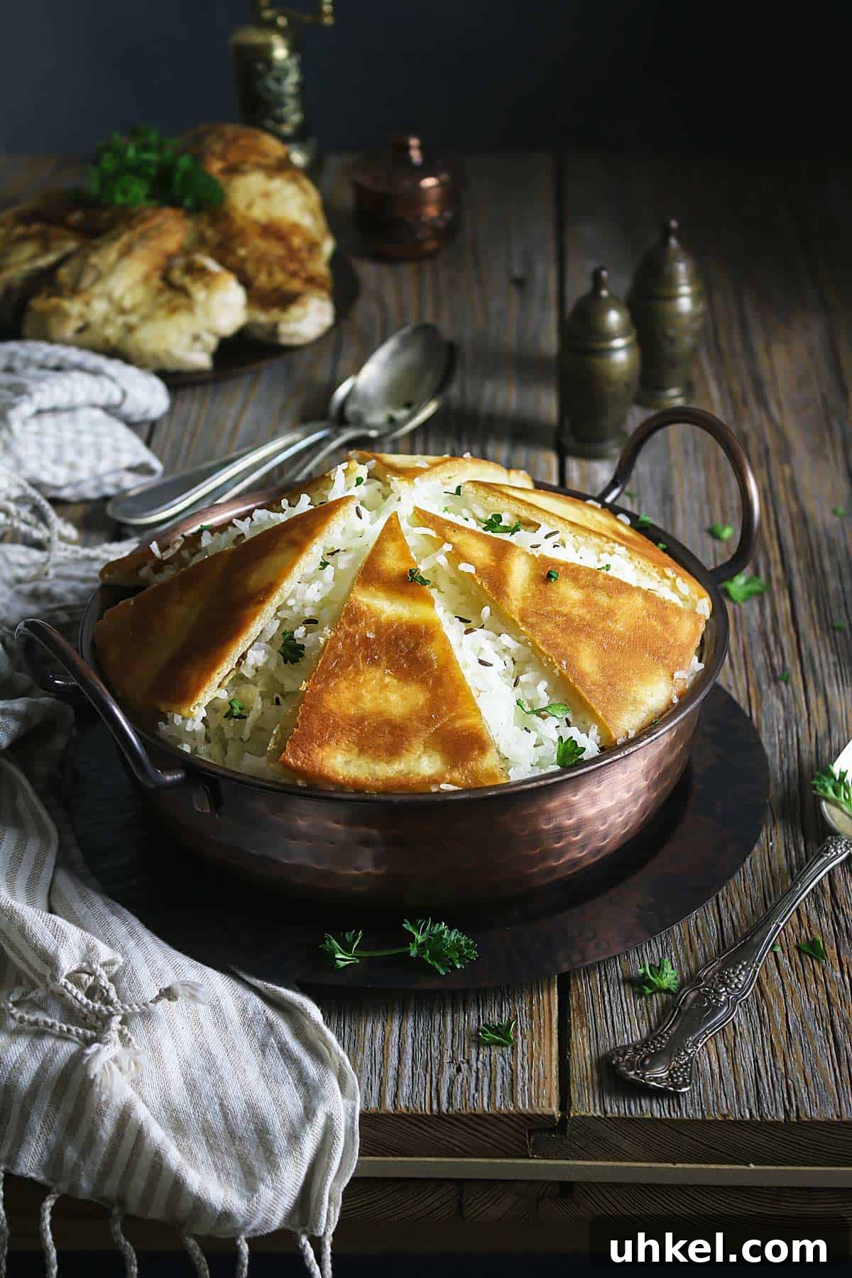 Crispy Tahdig with Naan Crust — Pan-Fried Persian Rice 11 Rice tahdig in a copper bowl with crispy naan bread sitting on a rustic wooden table with a kitchen towel.