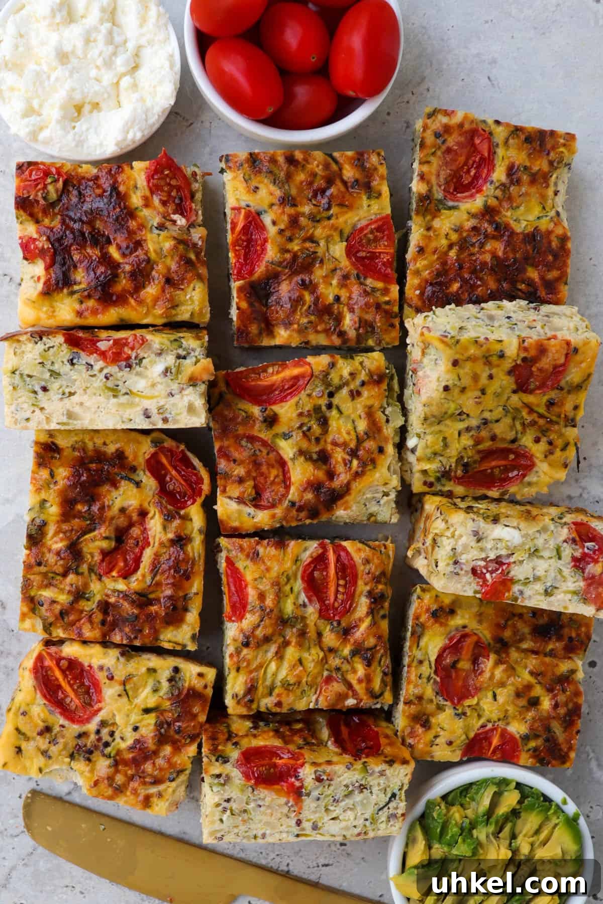 Cooked zucchini slice. Small dishes of cottage cheese and cherry tomatoes on the top side for decoration. Gold knife and and mashed avocado on the bottom.