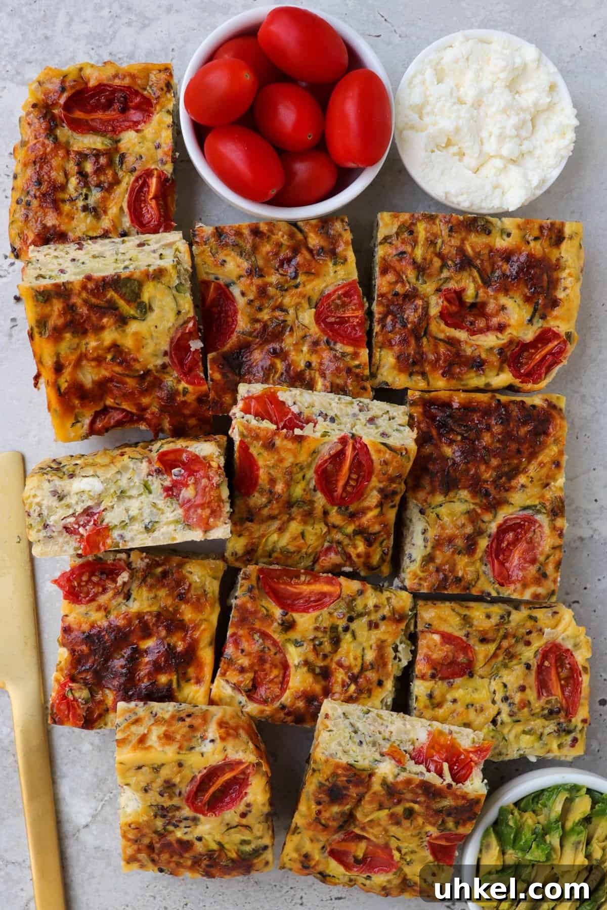 Cooked zucchini slice. Small dishes of cottage cheese and cherry tomatoes on the top side for decoration. Gold knife on left side and mashed avocado on the bottom.