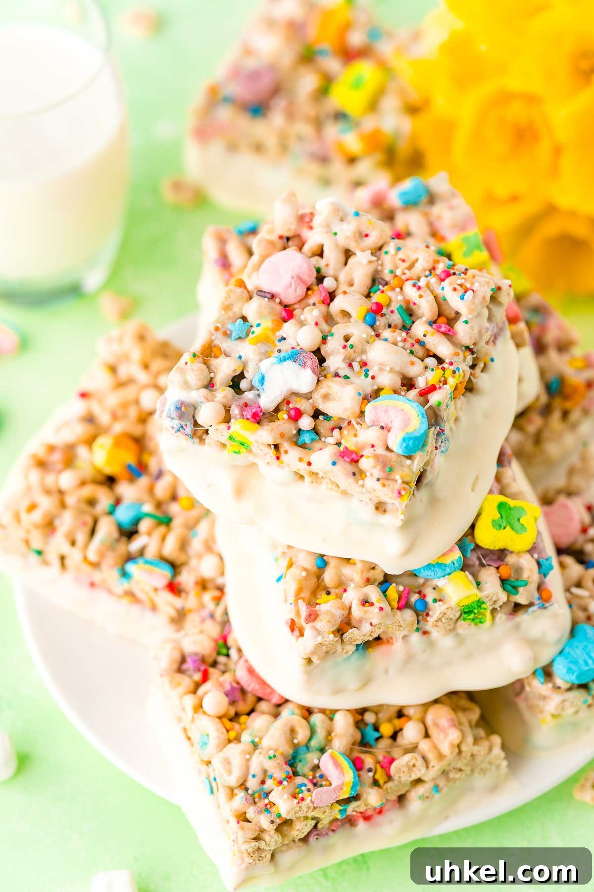 Lucky Charms Treats arranged on a white plate with a glass of milk and daffodils in the background.