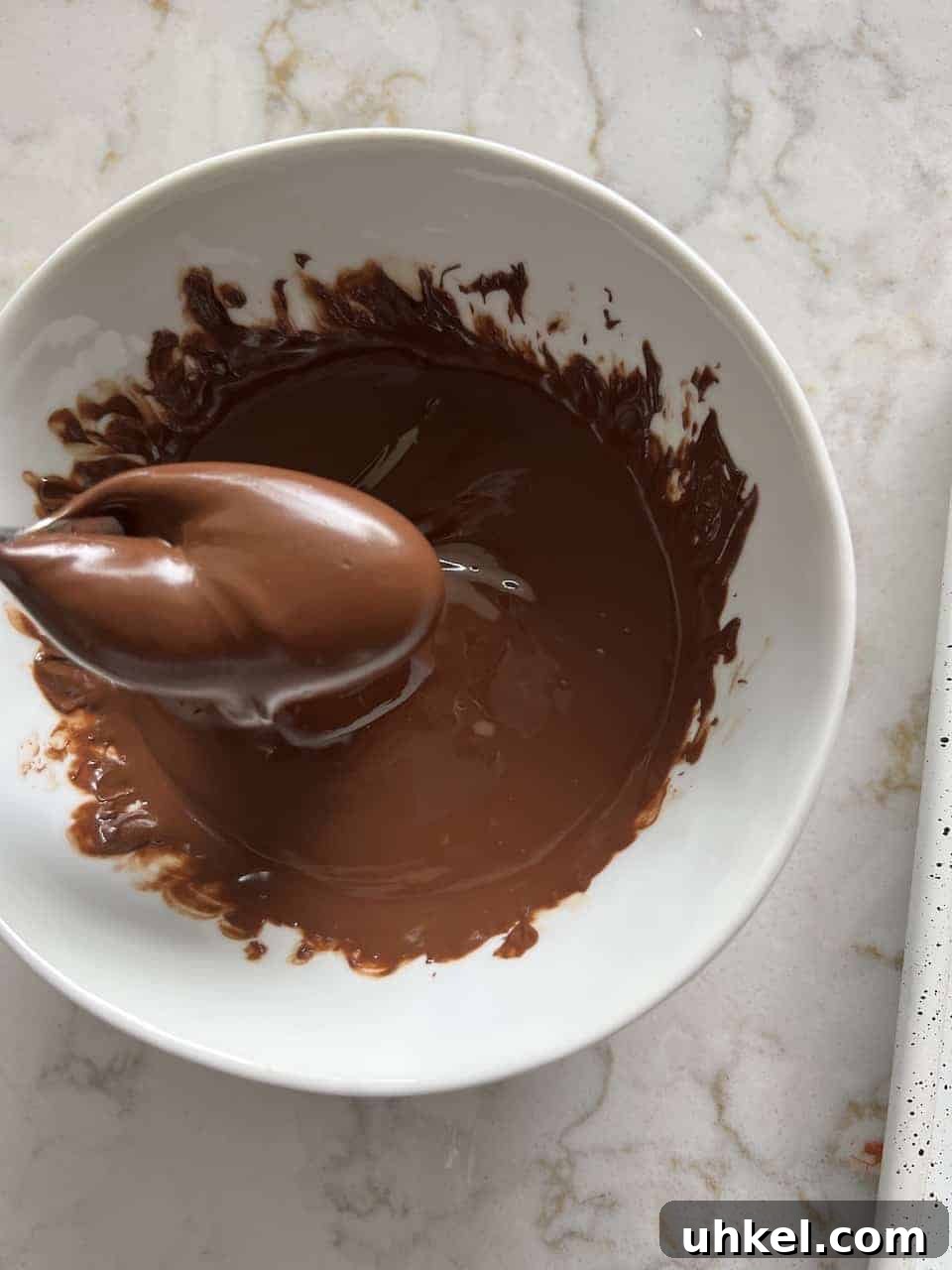 Vegan No-Bake Chocolate Peanut Butter Krispie Balls 7 process of melting chocolate in a small white bowl against a white marble surface