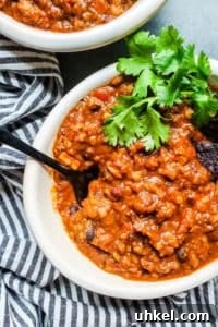 This Crockpot Vegetarian Chili is packed with lentils, beans, and veggies for the perfect combo of healthy and delicious. Slow cooker, Instant Pot and Stove Top instructions included. Chili in a white bowl on a blue counter with black spoon sticking out.