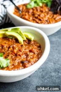 Vegetarian chili served with cilantro and avocado. Two white bowls of vegetarian chili on a blue counter with cilantro and avocado on top.