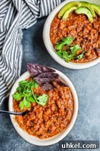 Served vegetarian chili. Two white bowls of veggie chili on a blue counter with a striped towel next to them.