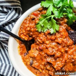 Hearty Crockpot Vegetarian Chili Recipe for Busy Nights 3 Chili in a white bowl on a blue counter with black spoon sticking out.