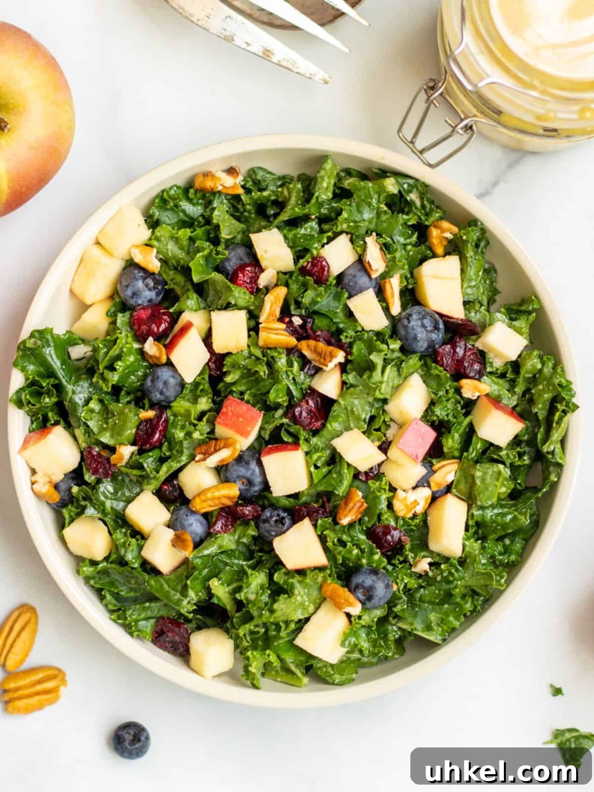 Kale Salad Kale salad with apples, berries and nuts in bowl with pecans and apples in background.