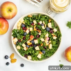 Crisp Kale and Apple Salad with Maple Dijon Dressing 2 Kale salad with apples, berries and nuts in bowl with pecans and apples in background.