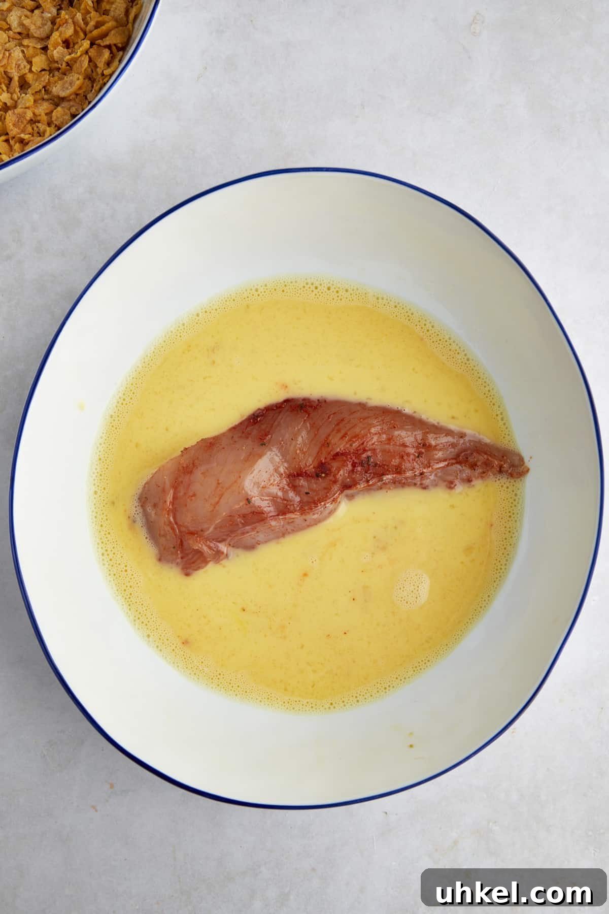 Raw seasoned chicken in a bowl of egg wash.