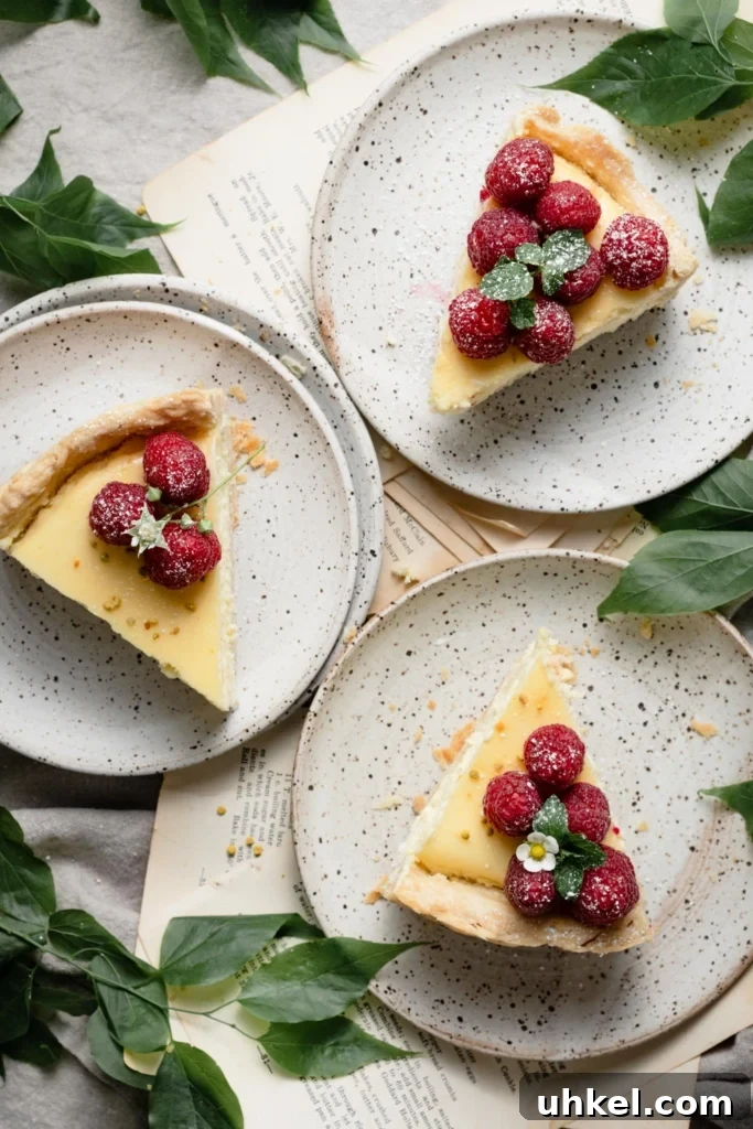 Lemon Curd Cheesecake Recipe with Zesty Citrus Topping 3 Three slices of lemon cheesecake topped with raspberries on three speckled plates.