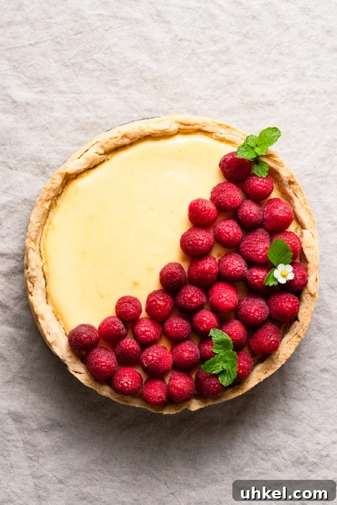 Lemon Curd Cheesecake Recipe with Zesty Citrus Topping 4 Overhead view of a lemon cheesecake topped with fresh raspberries inside a pie crust.