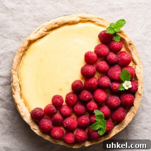 Lemon Curd Cheesecake Recipe with Zesty Citrus Topping 5 Overhead view of a lemon cheesecake topped with fresh raspberries inside a pie crust.