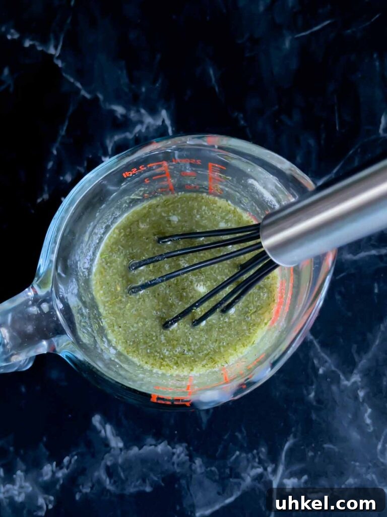 Tangy Dill Pickle Chex Mix Snack Recipe for Parties 5 Seasoning mix for Dill Pickle Chex mix in a glass measuring cup on a dark surface.