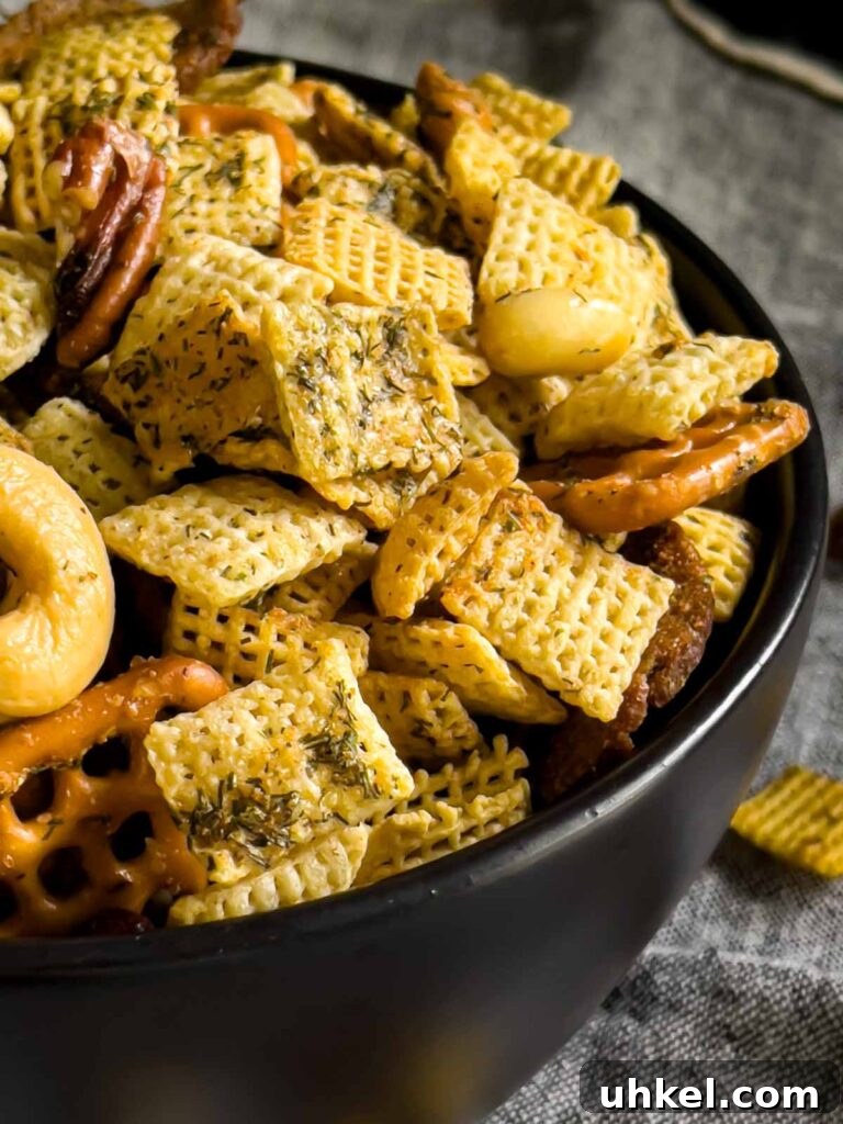 Tangy Dill Pickle Chex Mix Snack Recipe for Parties 8 Dill Pickle Chex Mix in a small dark bowl on a light linen napkin.