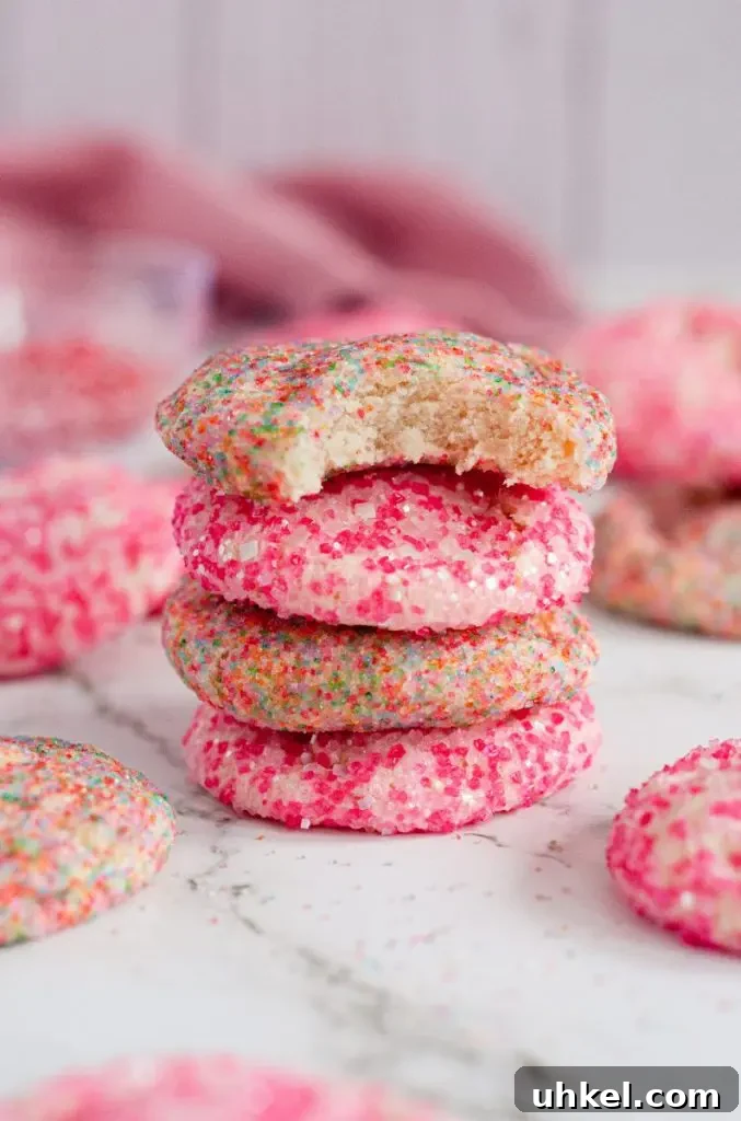 A stack of four sparkle sugar cookies that are covered in bright colorful sparkly sprinkles. The top cookie has a large bite taken out of it.