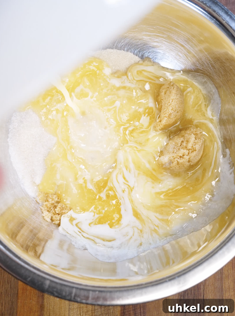 Melted butter being poured over granulated and brown sugar in a stainless steel bowl, the first step to creating shiny, crackly brownie cookie tops.