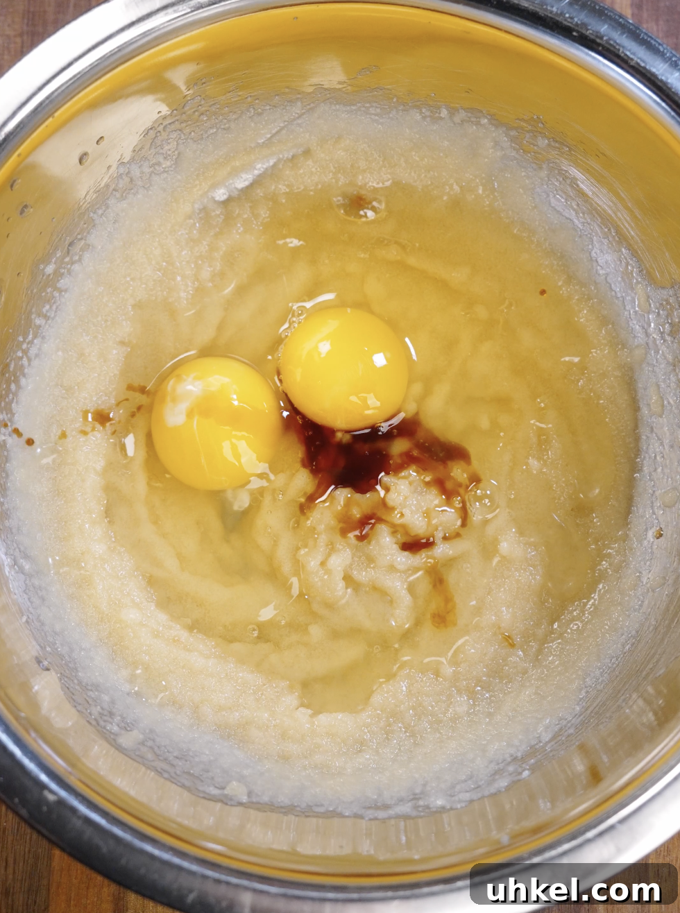 Eggs and vanilla extract added to the glossy butter and sugar mixture before continued whisking to aerate the batter for shiny brownie cookie surfaces.