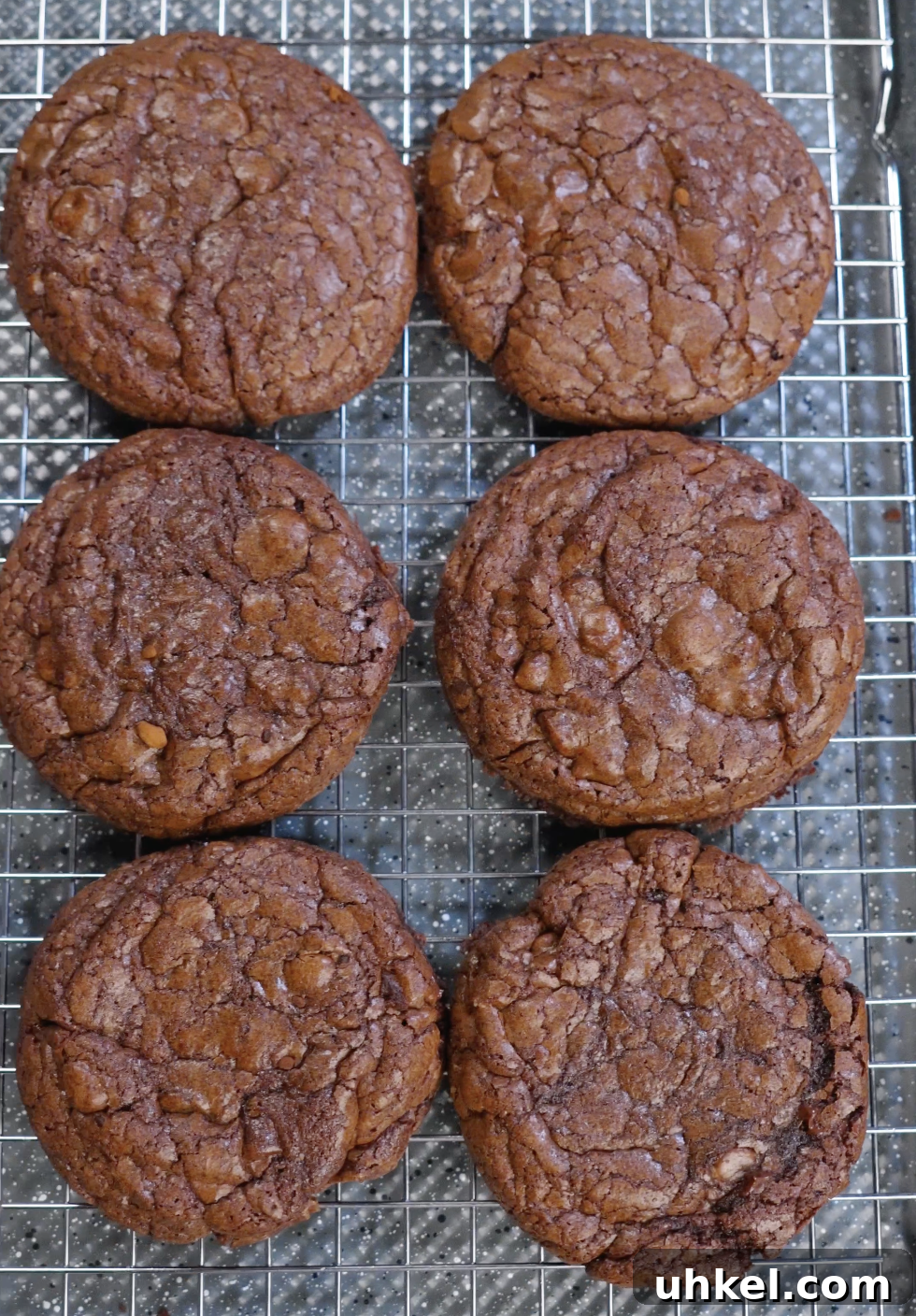 Freshly baked brownie cookies cooling on a wire rack with glossy crackled tops and set edges, showing proper sugar dissolution and aeration.