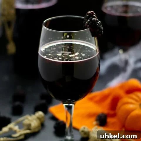 blackberry halloween sangria in a wine glass with fruit and pumpkins and skeletons on the table