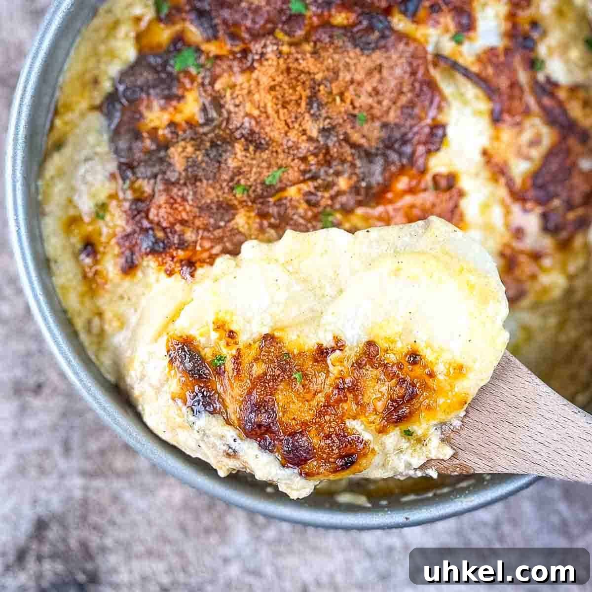 Crispy Cheesy Scalloped Potatoes Made in the Air Fryer 2 A wooden spoon lifting up a serving of air fryer scalloped potatoes out of a cake pan.